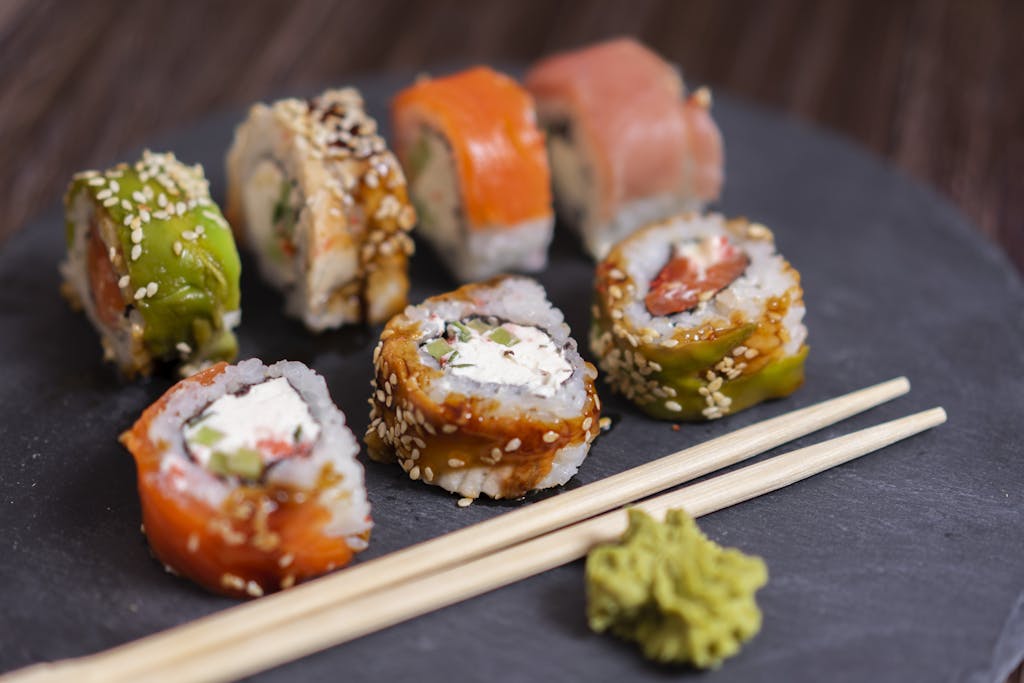 A colorful sushi platter with wasabi and chopsticks on a slate board.