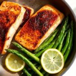 Golden-brown pan-seared salmon fillets with crispy skin, served alongside bright green sautéed asparagus with lemon wedges.